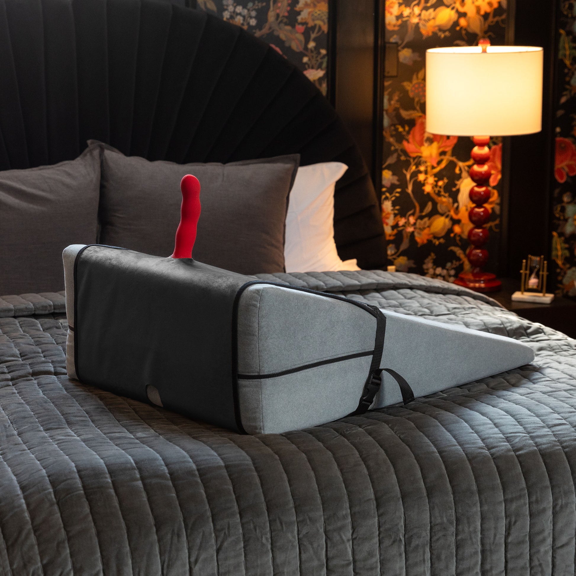 Grey Birdi Toy Mount, Bedroom Furniture by Liberator with black cover and a red vibrator in the holder sitting on a bed.