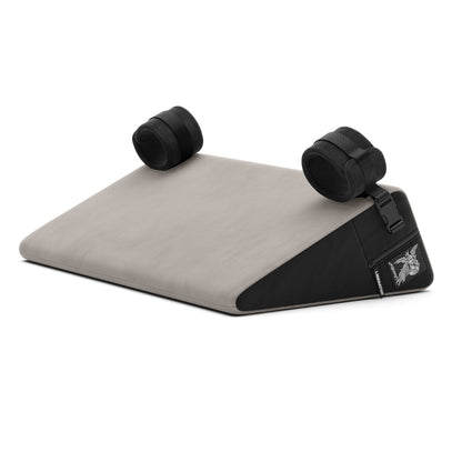 A grey Bondage Wedge, Bedroom Furniture by Liberator with handcuffs on a white background.