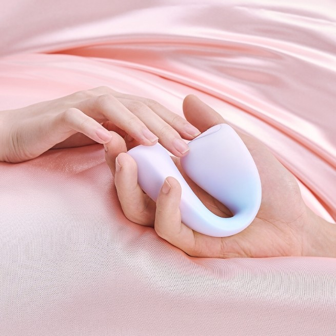 A lavender C-Tail G-Spot Vibrator, Bedroom Toy by Liberator in a hand sitting on pink silk.