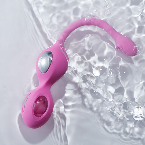 A pink Elektra-App-controlled E-Stim Kegel Training set laying in water against a white background.