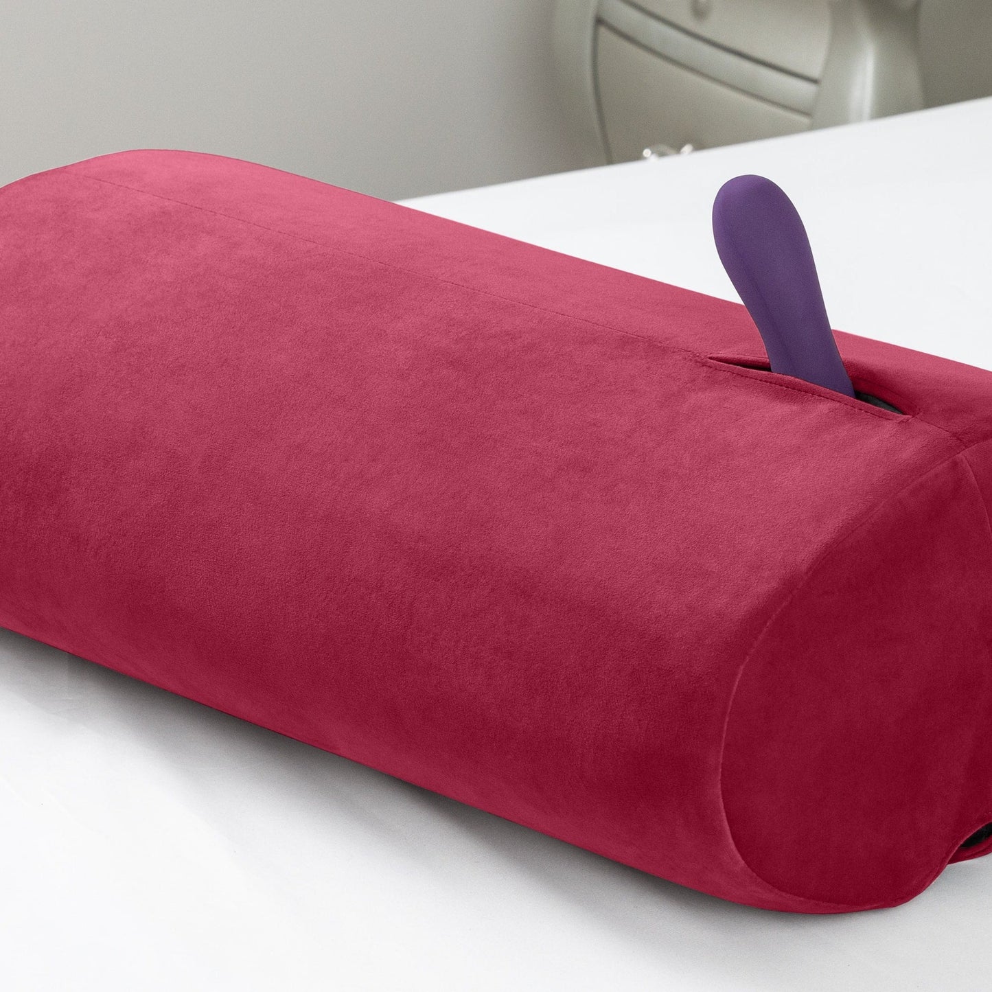 A merlot colored Wing Toy Mount, Bedroom Furniture by Liberator with a vibrator in the pocket against a white background.